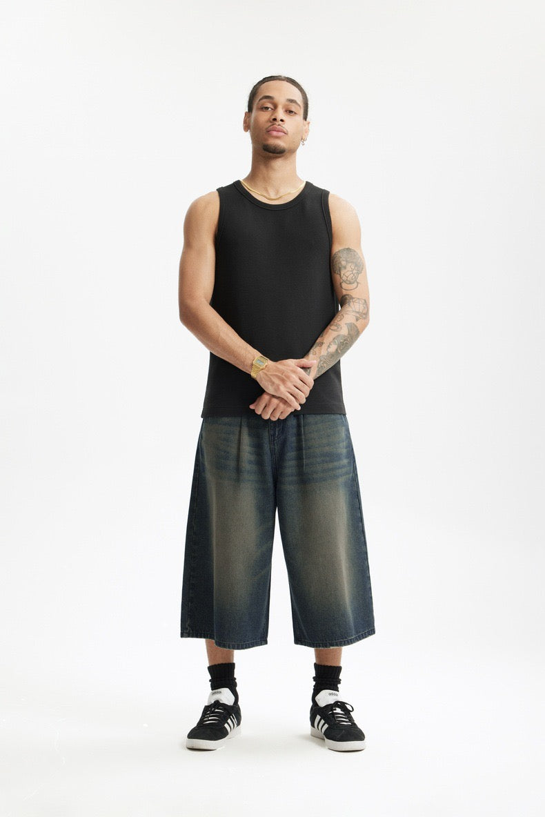 Model wearing dark wide-leg denim shorts and black tank top on white background