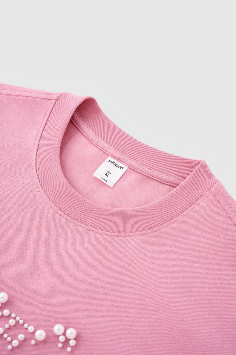 Pink crewneck tee with pearl rhinestone script detail on the chest, shown flat against a light background