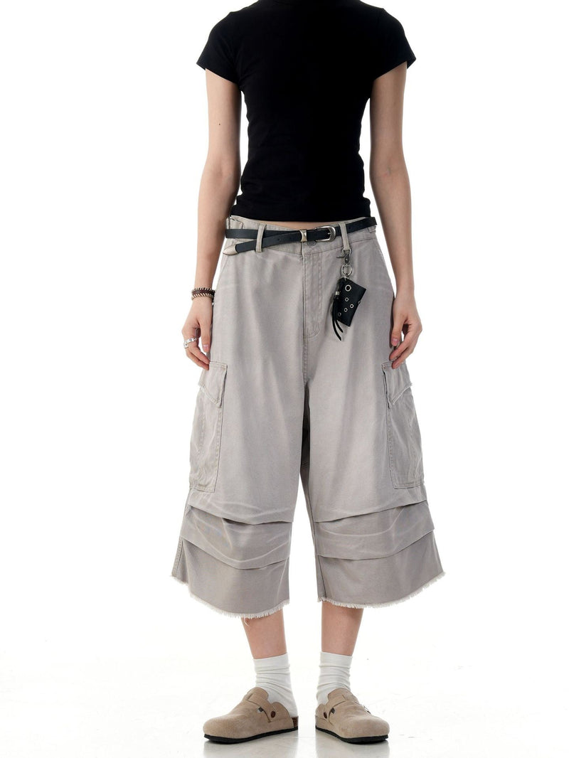 Beige cargo shorts on model, front view with wide legs, flap cargo pockets, and layered hems