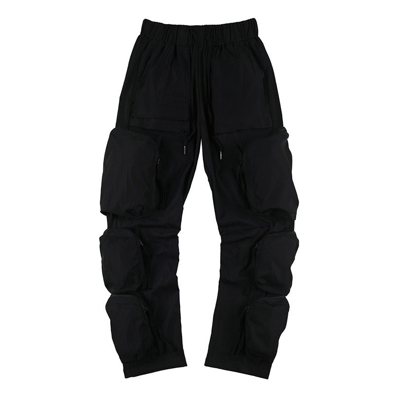 Black multi-pocket utility cargo pants with oversized 3D zip compartments stacked along the legs and elastic drawstring waist