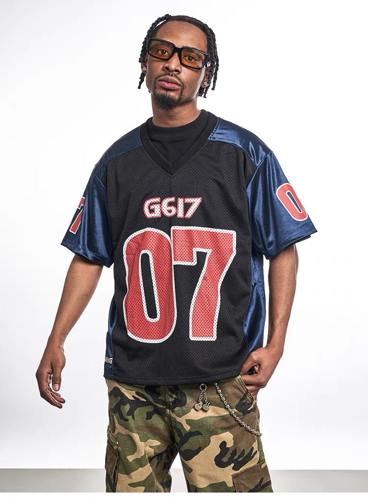 Black and navy oversized mesh jersey tee with red G617 07 varsity graphics on a male model, streetwear style