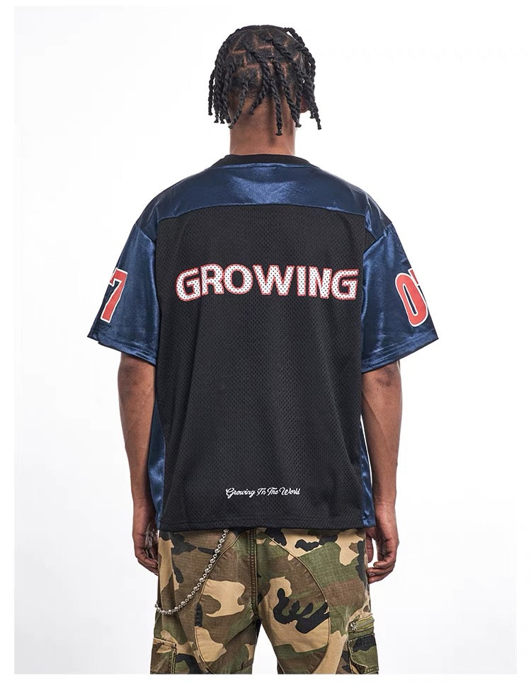 Oversized black and navy mesh jersey tee with varsity-style GROWING print on the back, worn with camouflage pants