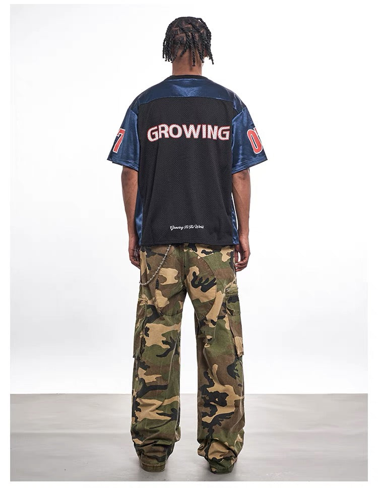 Oversized black mesh varsity tee with blue sleeves and bold GROWING lettering, styled with camo cargo pants