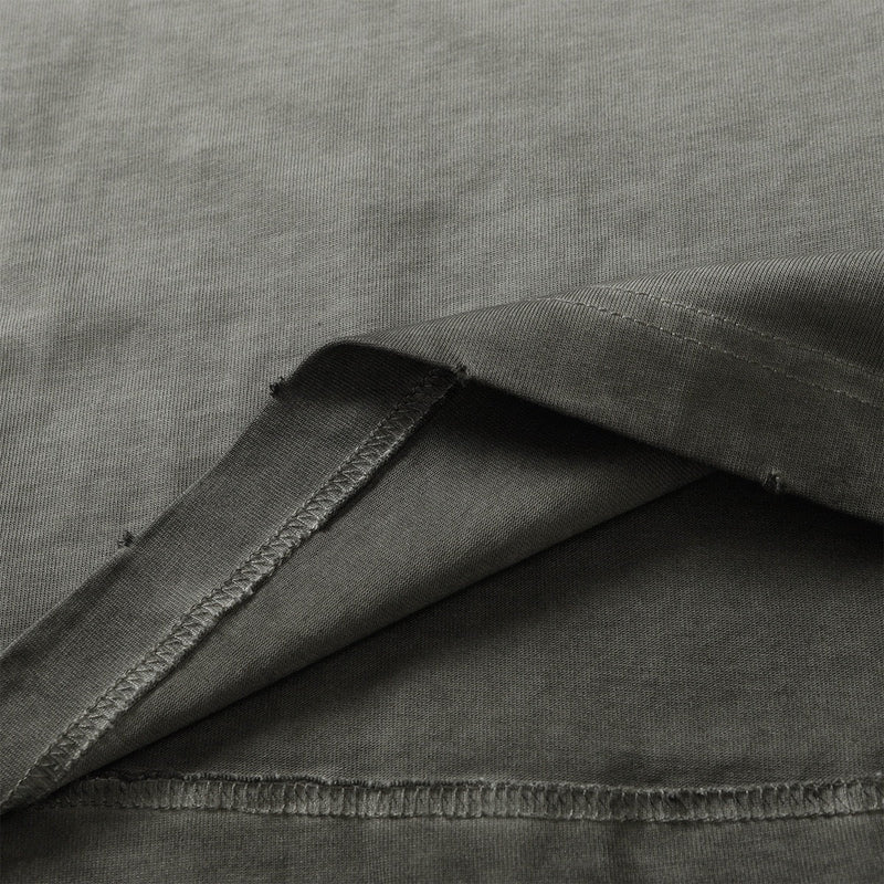 Close-up of a washed olive green cotton tee with distressed panel seams and raw-edge stitching detail