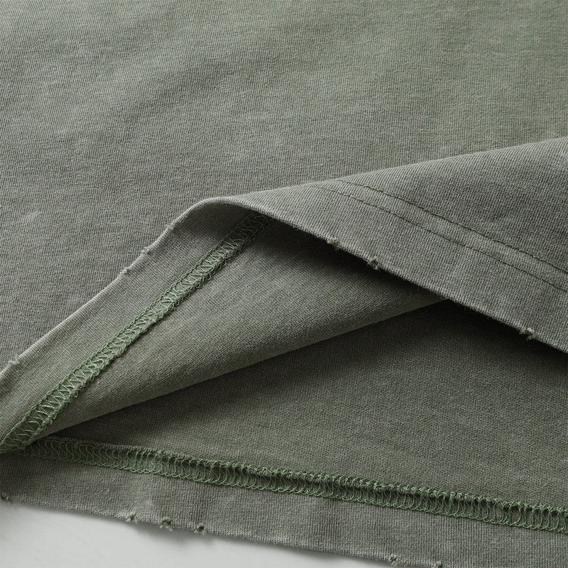 Close-up of olive green washed panel tee fabric with raw distressed hems and visible seam stitching