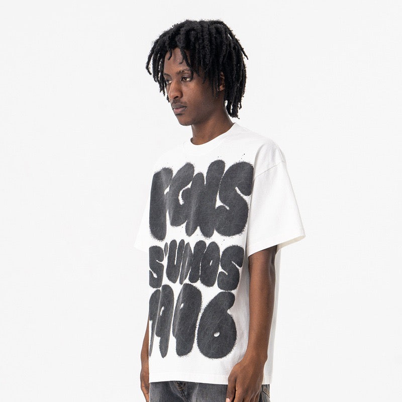 White oversized graphic tee with bold black 1996 graffiti-style print, worn by a male model on a clean studio background
