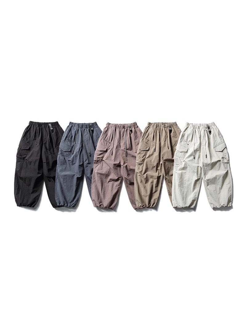 Off-white lightweight nylon cargo pants with elastic drawstring waist, flap pockets, and gathered ankle cuffs on a white back