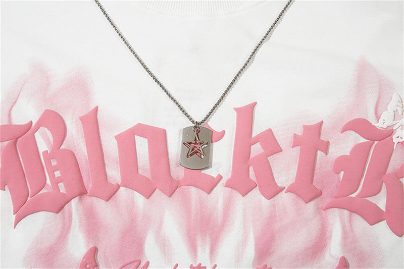 Close-up of a white graphic tee with pink gothic lettering and a silver star pendant necklace hanging over the chest