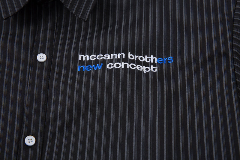 Front chest close-up of black pinstripe shirt with embroidered logo text and buttons