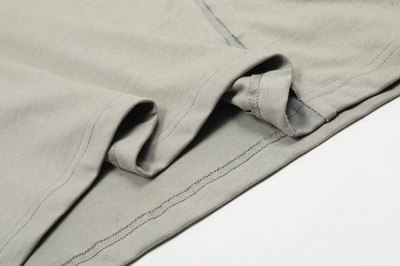 Close-up of a light gray cotton tee hem with exposed seams, asymmetric stitching, and folded sleeve detail