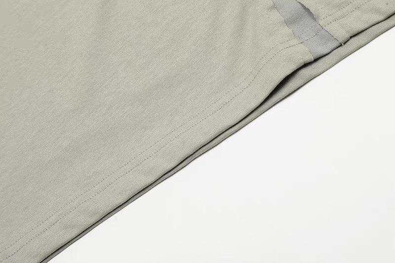 Close-up of a light gray minimalist cotton tee with asymmetric stitching and deconstructed seam detail