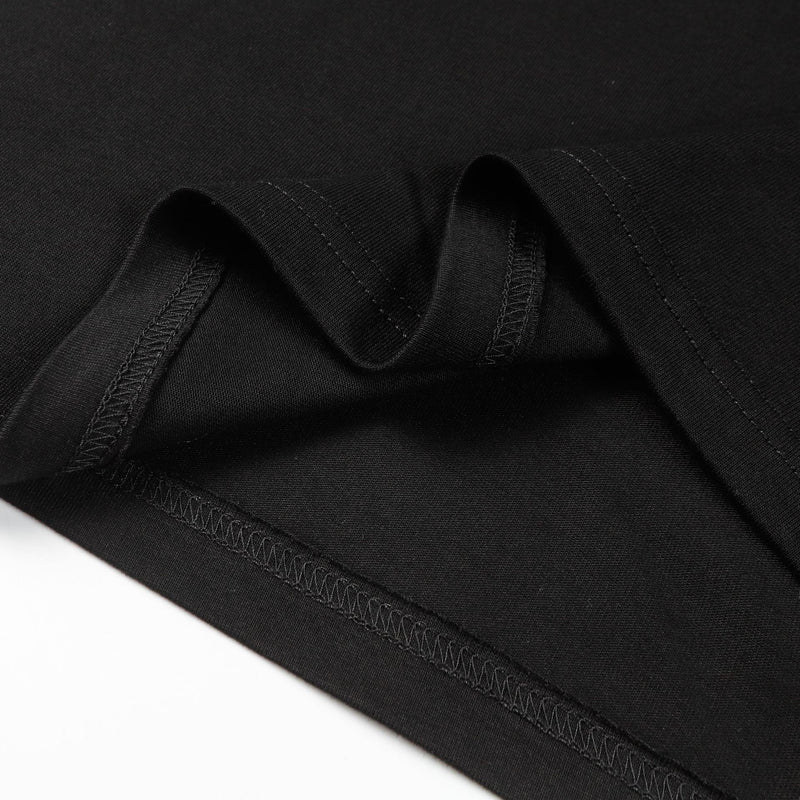 Close-up of black oversized tee fabric with visible hem stitching and layered seams on a minimalist white background