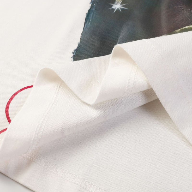 Folded white streetwear tee with a bold portrait graphic and red circular accent, showing stitched seams and soft fabric texture