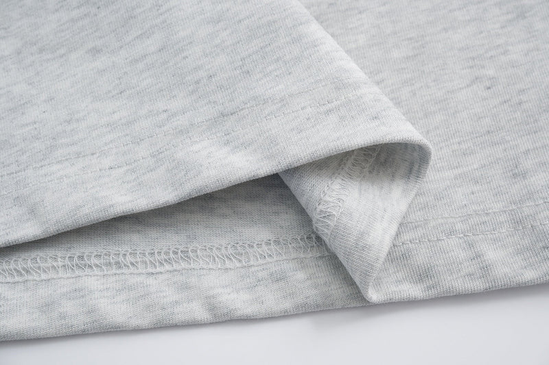 Close-up of light gray cotton tee hem with visible stitching and soft streetwear fabric texture