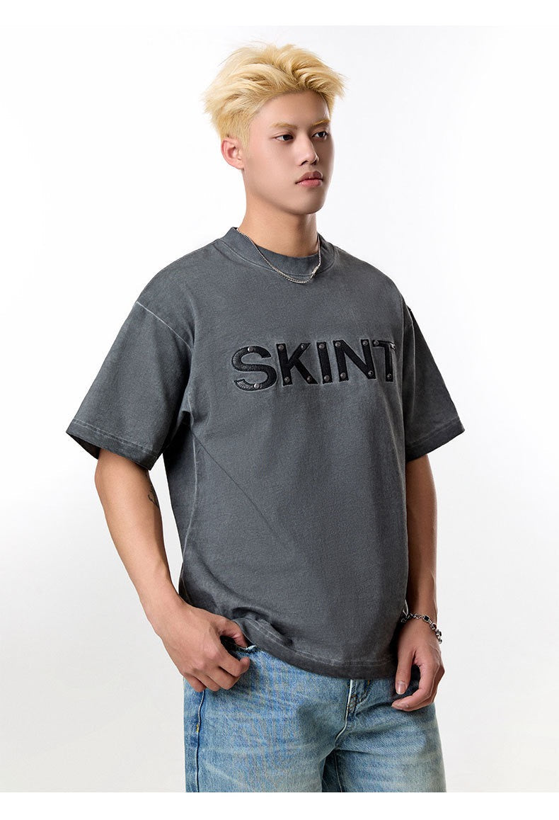 Man wearing a faded charcoal SKINT vintage washed tee with oversized fit and rivet detail, paired with light blue jeans