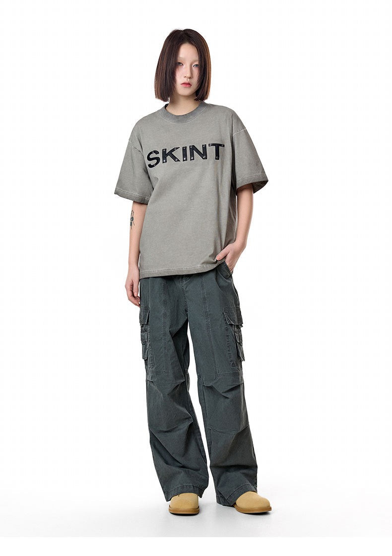 Model wearing a gray SKINT vintage washed oversized tee with wide-leg cargo pants and tan shoes on a white background