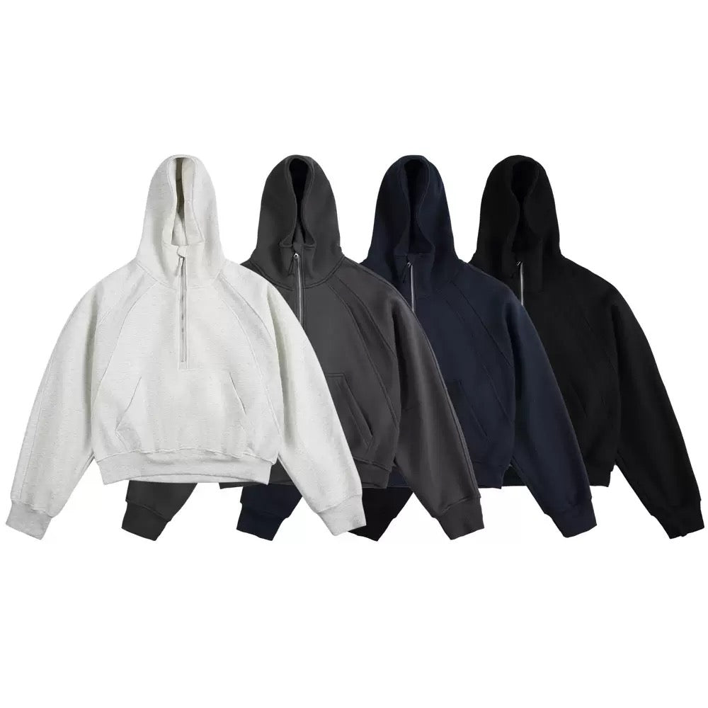 Four half-zip cropped hoodies displayed in light grey, charcoal, navy, and black colorways on a white background