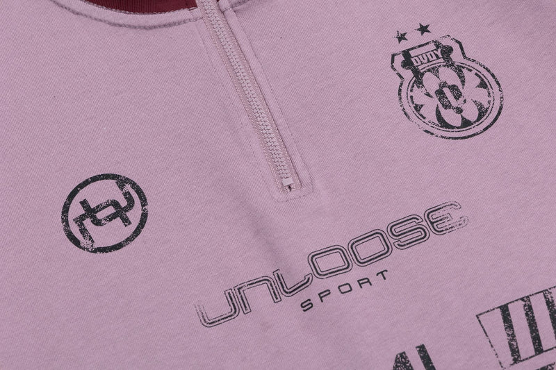 Pink oversized streetwear tee with half-zip collar and distressed black graphic prints across the chest