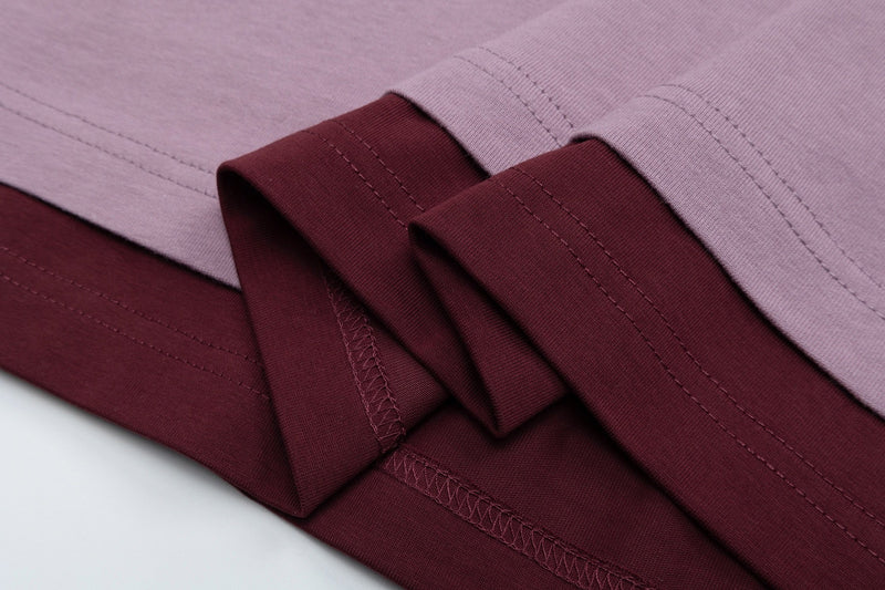 Close-up of folded oversized streetwear tee in lilac and burgundy with visible stitched hems and cuffs