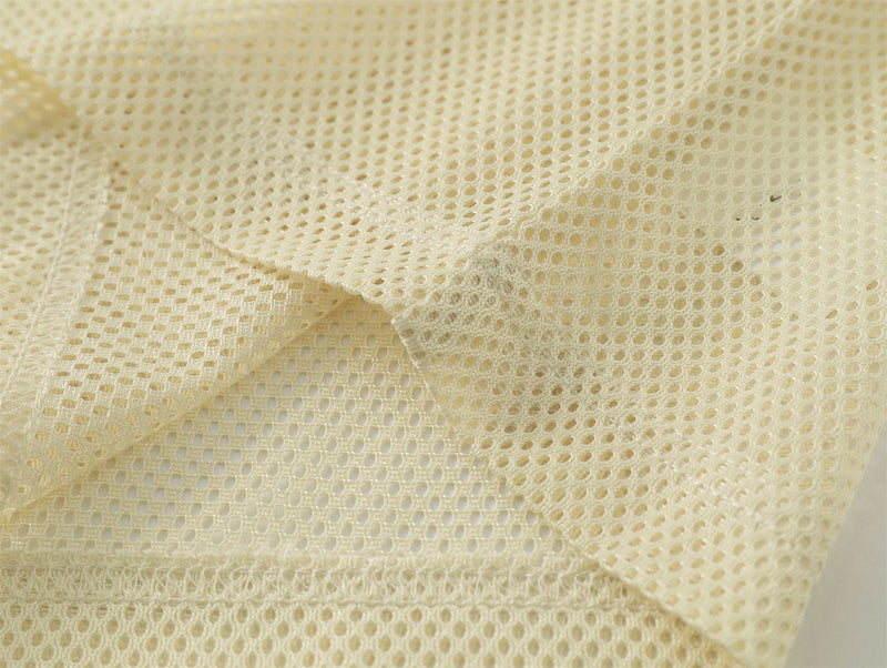 Close-up of cream mesh fabric with a sheer perforated texture and stitched hem on a Y2K streetwear tee