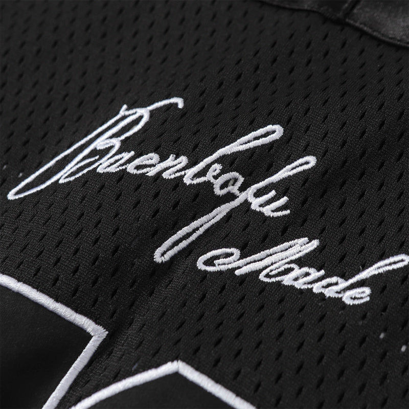 Black mesh football jersey with white embroidered script and star detail, close-up of streetwear fabric texture