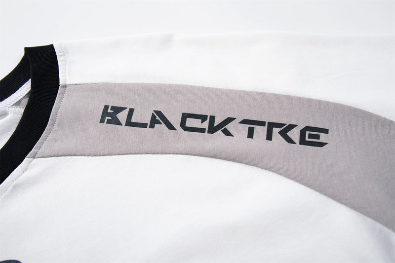 Close-up of a white and gray raglan streetwear tee with black trim and bold KLACTKG graphic on the shoulder