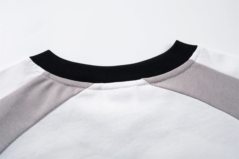 Close-up of a white and gray raglan streetwear tee with a black ribbed crew neckline and stitched shoulder seams