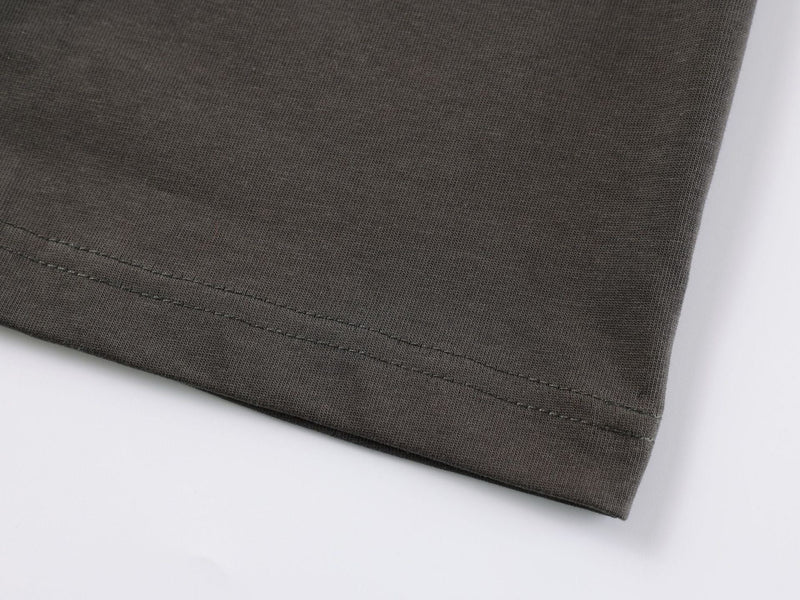 Close-up of an olive green tee hem with double-stitched seam on a clean white background
