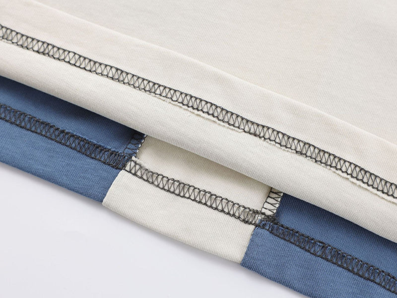Close-up of stacked color-block tee fabric in cream and blue with visible contrast stitching and seam detail