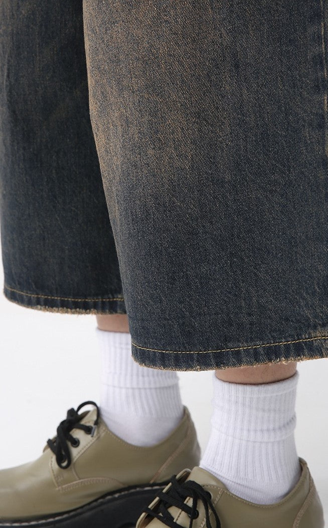 Close-up of wide-leg denim shorts hem with raw edge and white socks above shoes