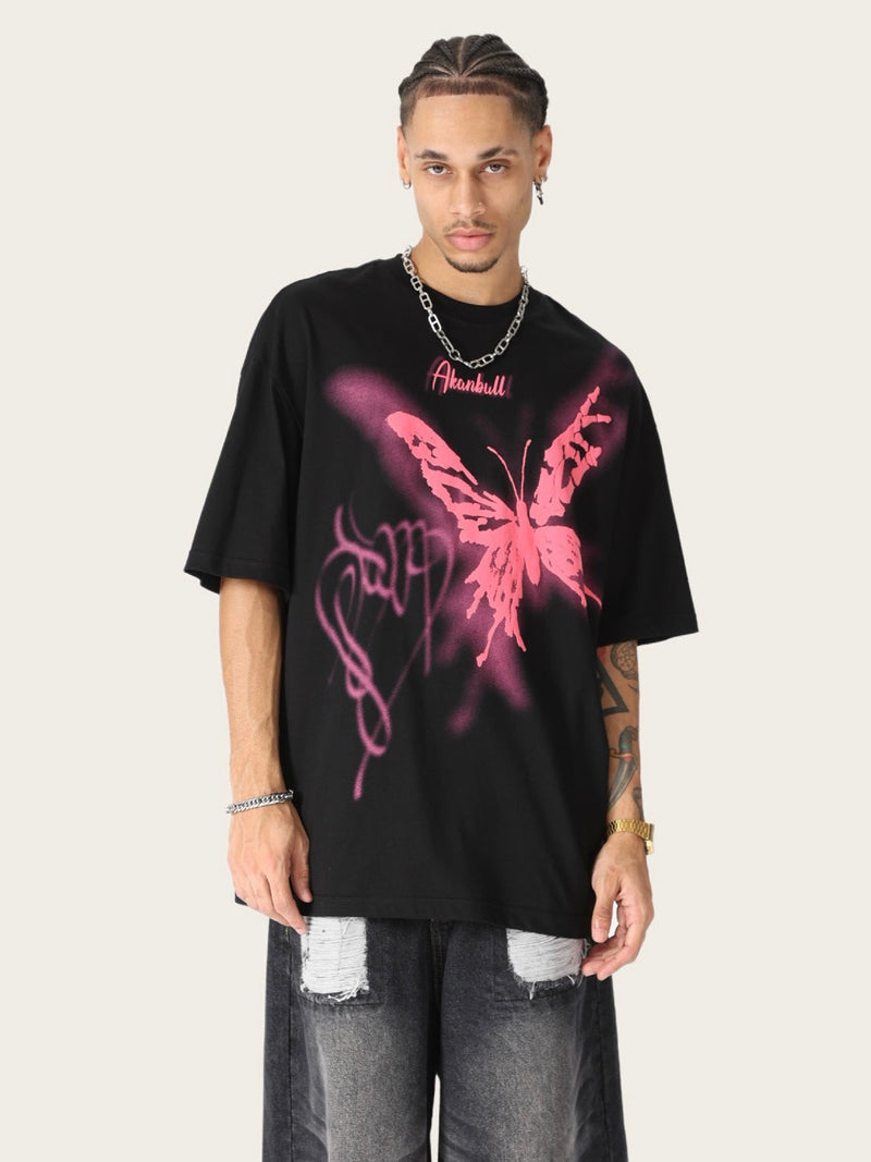 Black oversized streetwear tee with a pink graffiti butterfly graphic, worn with ripped jeans and chain necklace