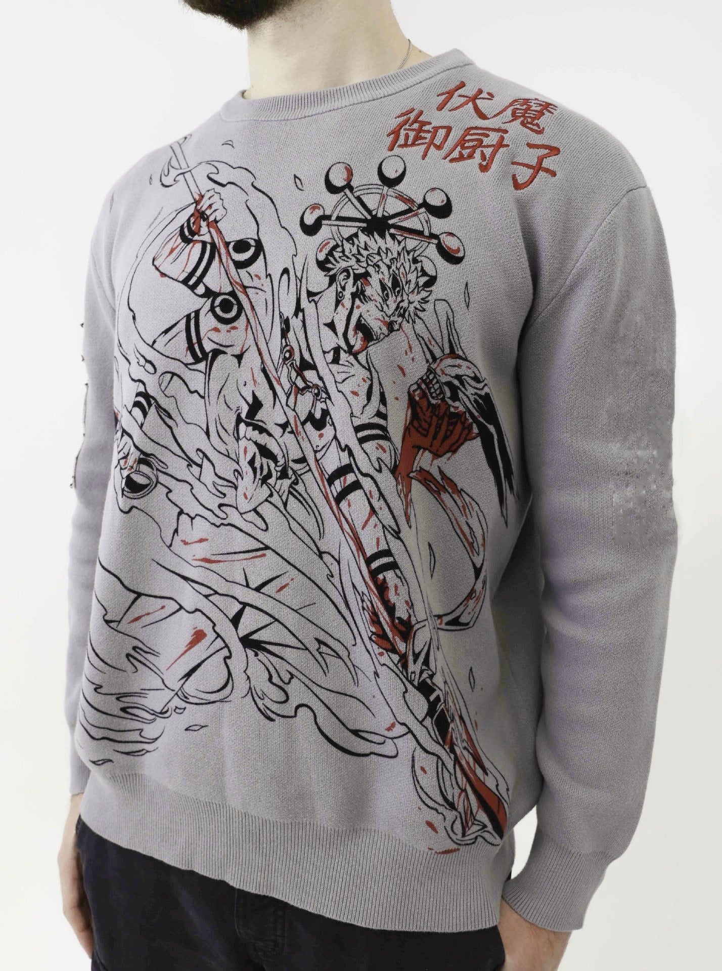 A person wearing a Jujutsu Kaisen Premium Knit Sweater with a Ryomen Sukuna Domain Expansion Jacquard Design in light gray, featuring black and red patterns plus Asian characters on the upper right, stands against a plain background with their face unseen.