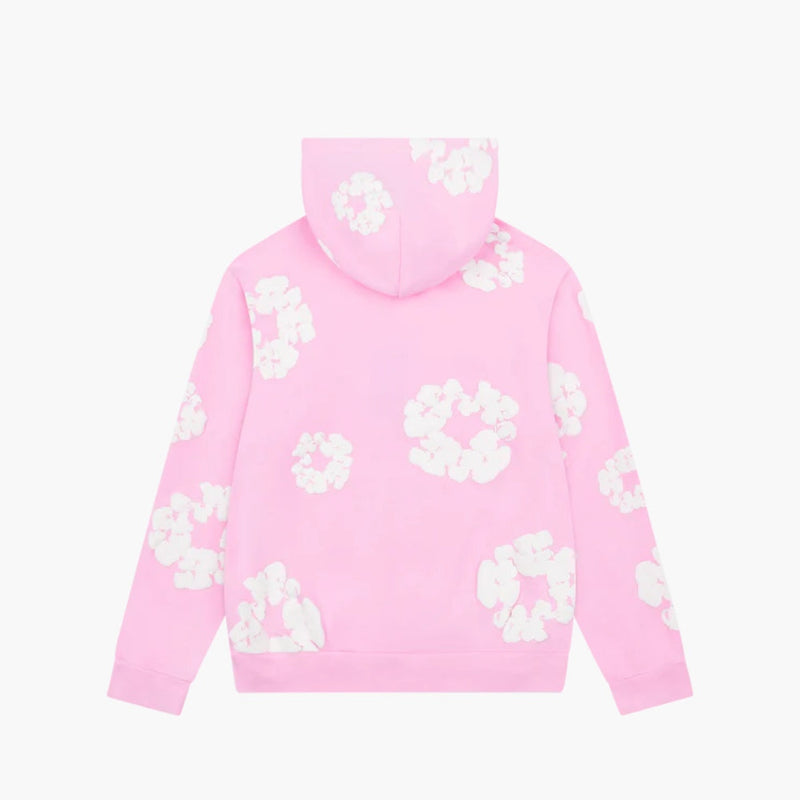 The Pink “Cotton Wreath” Denim Tears Hoodie is a light pink streetwear pullover with a hood, decorated with white floral prints on the back, sleeves, and hood. Displayed against a plain white background.