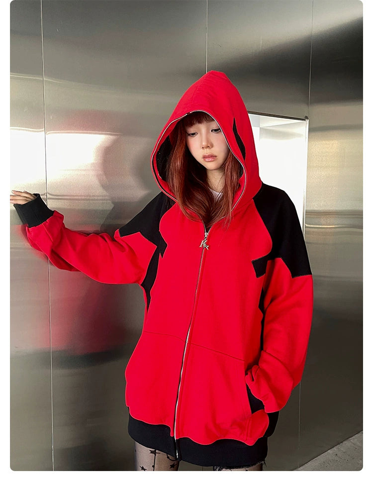 A person stands before a metallic wall, wearing an oversized Seakoff Deadpool-Inspired Hoodie. The red and black 400GSM zip-up sweatshirt exudes superhero style, with the hood drawn up as they gaze downwards, one hand on the wall. Its relaxed fit enhances its edgy charm.