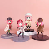 The Spy x Family Detective Anya PVC Figure Set includes four 14 cm figurines of Anya, each with pink hair and green eyes, in diverse outfits: beige coat, red cap, cream coat with beret, and brown jacket holding a magnifying glass. The movie version set features a soft pink backdrop.