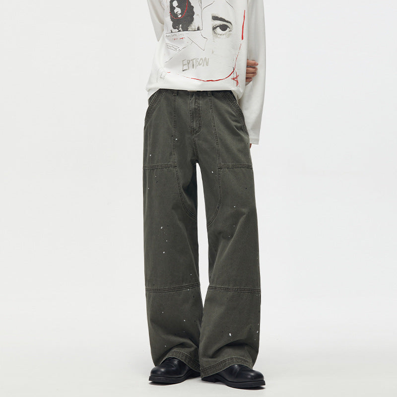 Men's baggy olive green paint-splatter deconstructed workwear trousers with wide straight leg and panel seam detailing