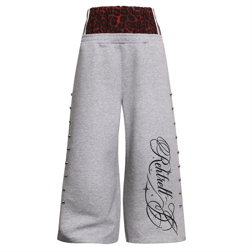Wide-leg sweatpants with red leopard print double waistband, silver ball studs along outer seams, and script graphic on lower