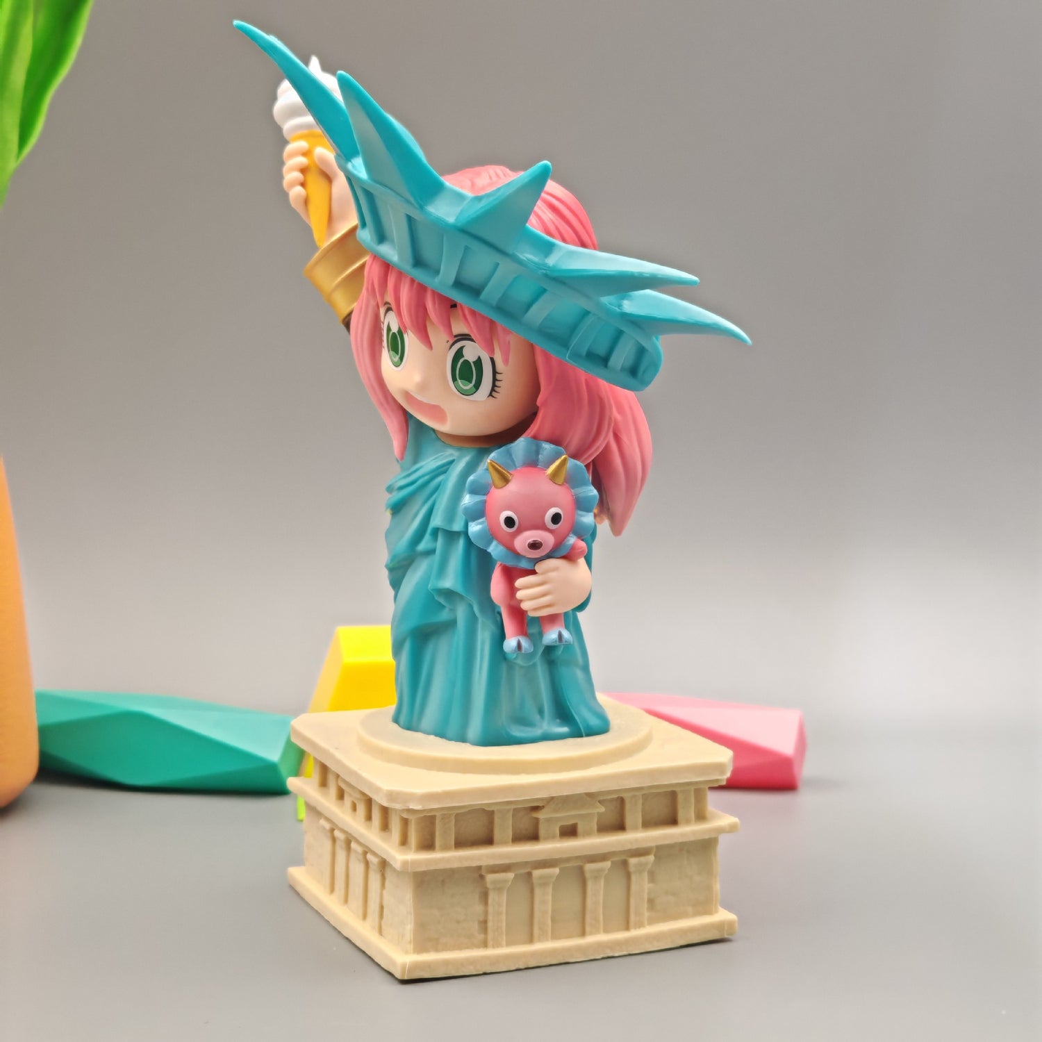 The Spy × Family Anya Forger Statue of Liberty PVC Figure, an 18.5 cm chibi-style figurine, features a pink-haired Anya holding an ice cream while wearing a blue crown and robe. She stands confidently on a base resembling the Statue of Liberty&