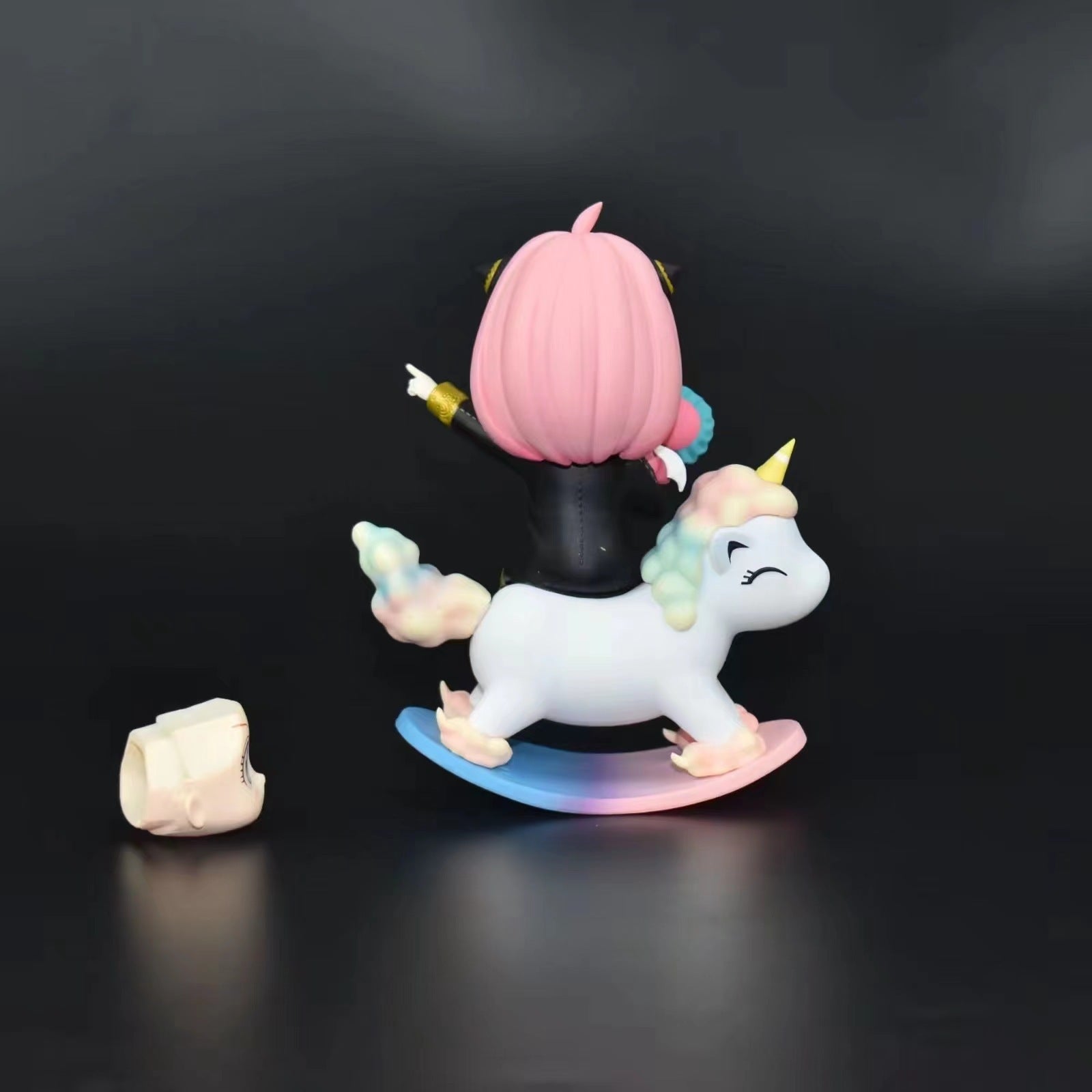 The Spy x Family Anya Forger PVC Figure features a pink-haired character on a pastel white unicorn with a rainbow base, yellow horn, and closed eyes. This whimsical 15 cm figure includes an interchangeable face expression and stands out against the black background.