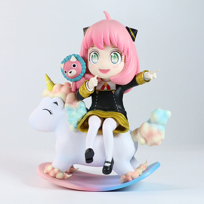 The Spy x Family Anya Forger PVC Figure (15 cm) portrays Anya with pink hair and cat-like ears, dressed in a black dress with gold accents, sitting on a pastel unicorn rocking horse. Featuring an interchangeable face expression, it embodies charm alongside her tiny doll.