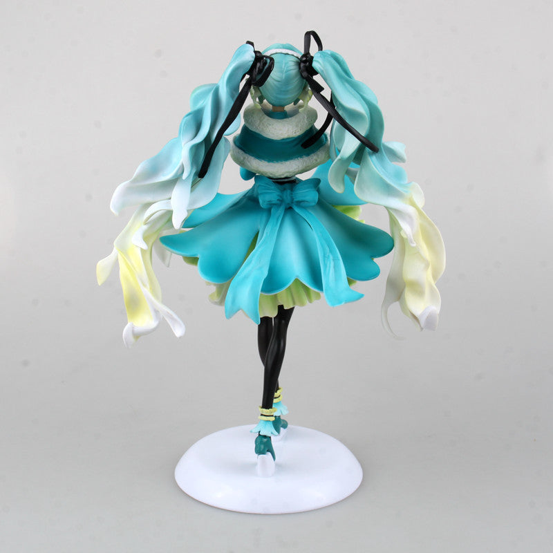 The Hatsune Miku 1/7 Scale 28cm PVC Figure features elegant teal and white flowing hair, a turquoise ruffled dress with a large back bow, standing on a white circular base with arms raised.