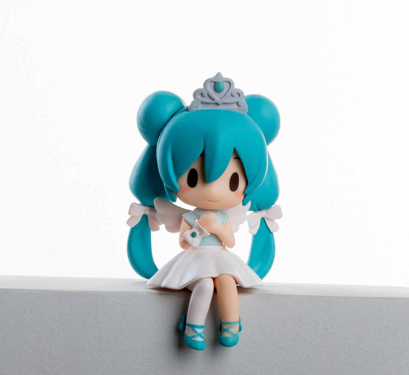 A 7.5cm chibi-style PVC figure from the Hatsune Miku Prayer Hugging Angel Princess set features an angelic character with teal hair, a tiara, a white dress with a bow, and teal shoes, holding a small white item on a white surface. The background is plain white.