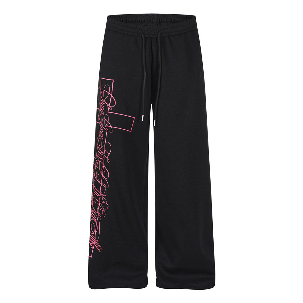 Black wide-leg sweatpants with neon pink cross and cursive script graphic print on the leg