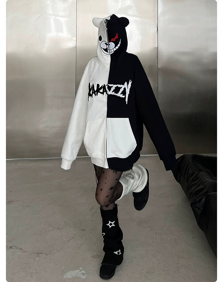 A person in a half-black, half-white Seakoff Monokuma-Inspired Hoodie, featuring a bear face on the hood, stands on one leg indoors near a metallic wall. The look is completed with black star-patterned tights and leg warmers, perfect for Danganronpa fans.