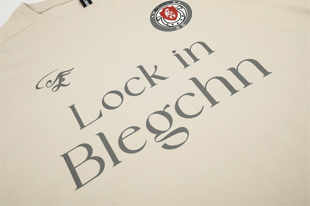 Beige tee front print detail with chest logo, crest patch, and large Lock in Blegchn text