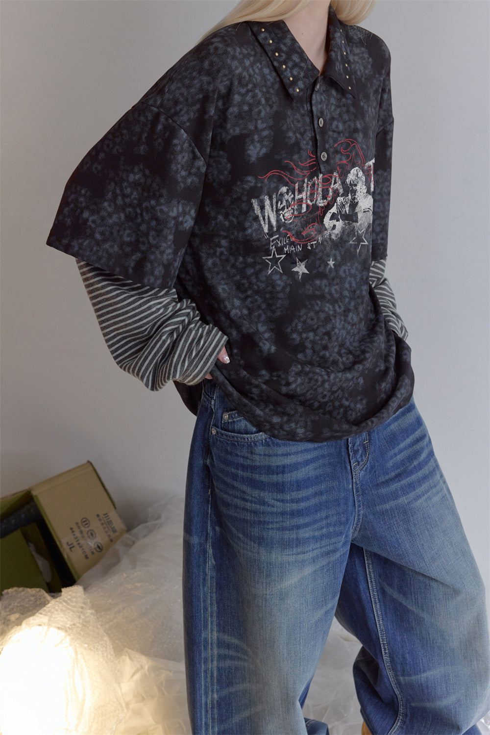 Angled view of a dark mottled faux-layered polo shirt with striped sleeves and red-and-white chest graphic
