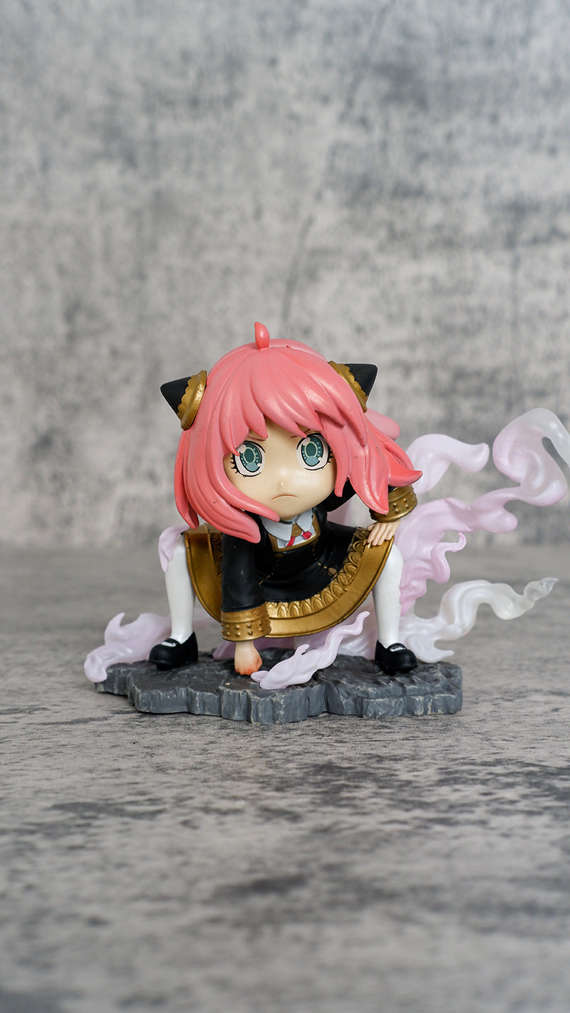 The Spy × Family Anya Forger PVC Figure is a chibi-style collectible featuring a pink-haired character with cat ears and large green eyes. She wears a black outfit and stands on a stone-like base with swirling pink mist, all set against a simple gray background.