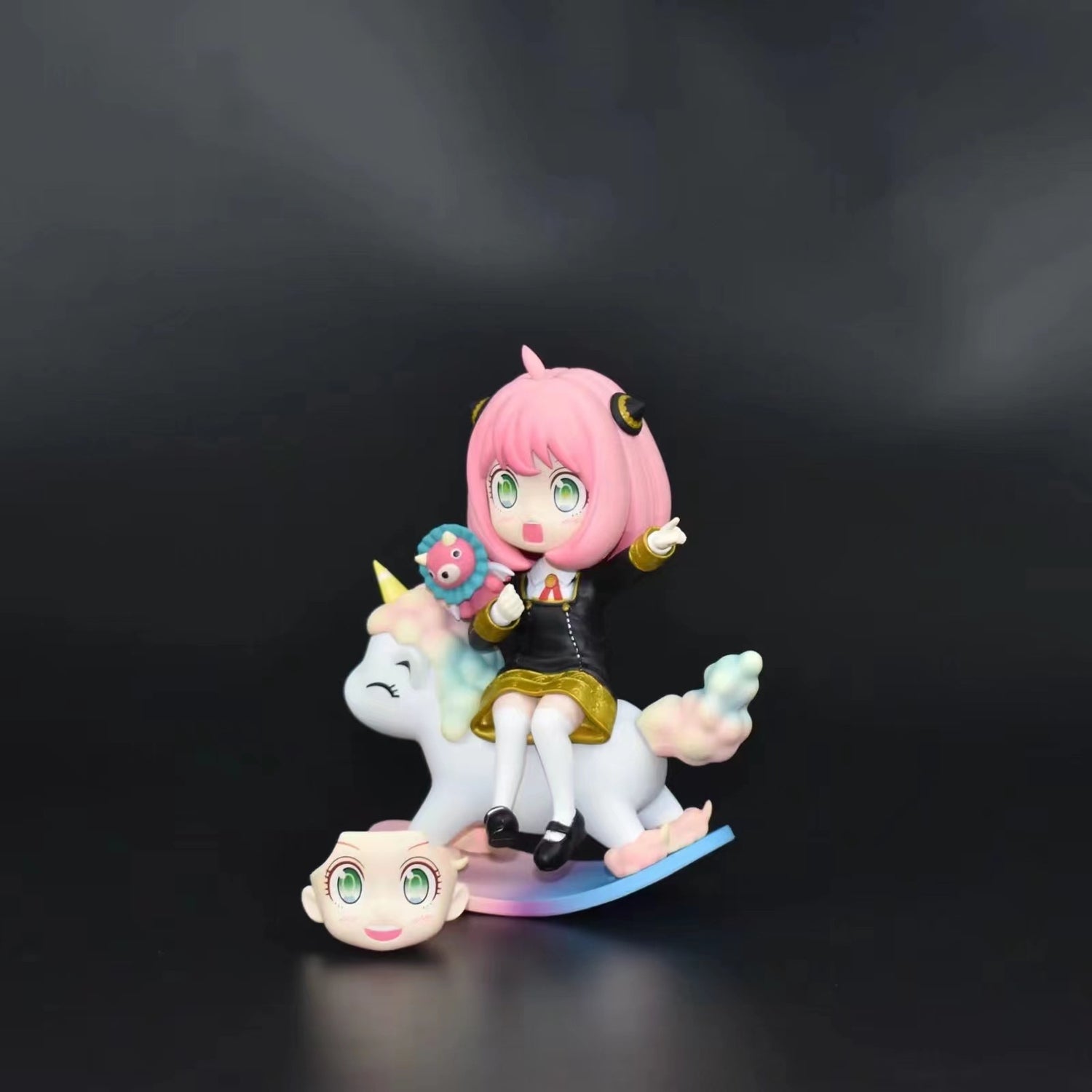 The Spy x Family Anya Forger PVC figure, by Spy × Family, features a pink-haired character in a black outfit, seated on a unicorn rocker. This 15 cm enchanting piece includes an interchangeable face expression with large eyes and a small accessory.