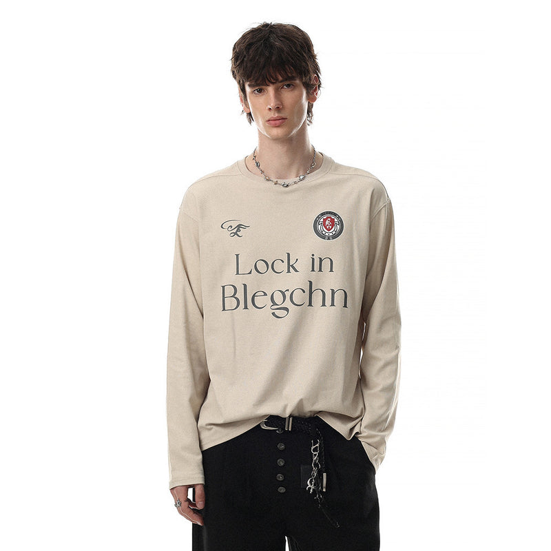 Beige long sleeve crew neck tee worn by a model, front view with chest graphic and logo patch