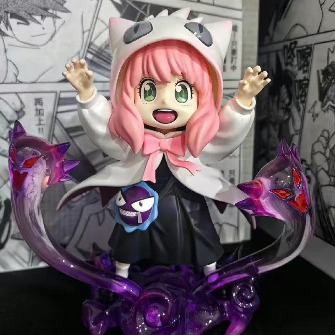 This chibi-style PVC figurine of Anya Forger from Spy × Family features pink hair and a white hoodie with cat ears, reminiscent of Gengar cosplay. Standing on a purple swirling base, her exaggerated eyes exhibit manga charm, with cartoonish eyes and raised arms accentuating the design.